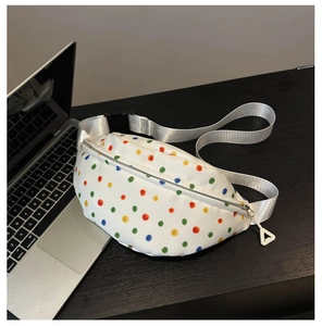 Close-up of white crossbody chest bag with colorful polka dots and woven strap on wood desk