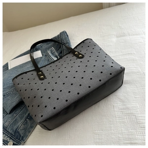 Detail of grey star print tote bag with black faux leather handles and gold hardware
