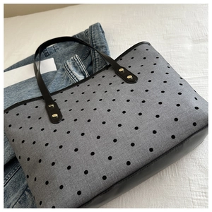Detail of grey canvas tote with black polka dots, leather handles and golden studs