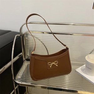 Brown faux leather baguette bag featuring a gold metal bow buckle and a retro shoulder strap