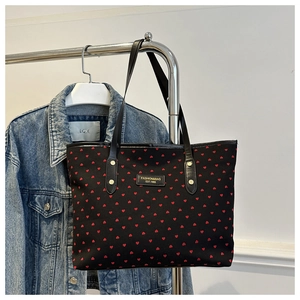 Détail d'un sac cabas noir à motifs cœurs rouges et attaches de sangle en métal