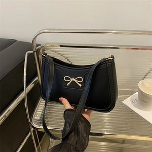 Detail of a black crescent baguette bag with a decorative gold bow metal buckle and thin strap
