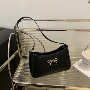Detail of a black leather underarm bag featuring a golden metal bow buckle in a studio setting