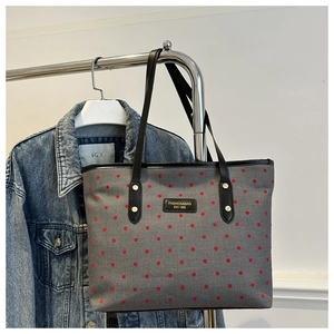 Gros plan d'un sac cabas gris à pois rouges avec des anses en cuir noir suspendu