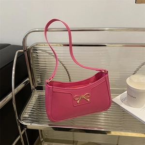 Detail of a bright pink shoulder bag featuring a gold bow buckle on a glass shelf