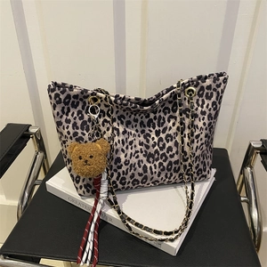 Große Shopper-Tasche mit Leopardenmuster, Metallkette und Bären-Anhänger auf Stuhl