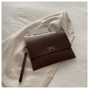 Detail of dark brown envelope clutch with silver bow accent on beige blazer background