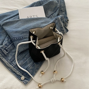 Minimalist black corduroy bucket bag with white drawstring and gold metal accents