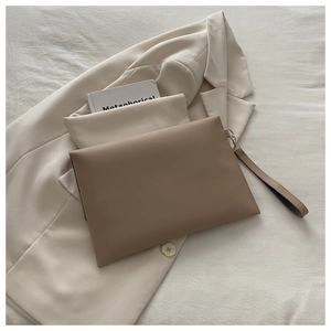Minimalist beige envelope clutch bag with leather strap next to a blazer and book