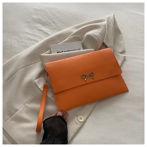 Detail of orange leather envelope clutch bag with silver bow buckle and hand strap