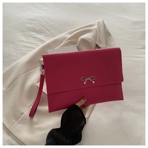 Detail of rose red envelope clutch bag featuring a silver bow and wrist strap on beige blazer