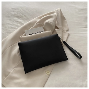 Detail of matte black minimalist envelope clutch bag with leather wristlet strap on fabric