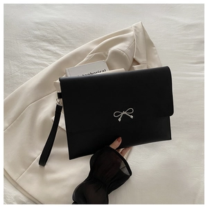Close-up of black envelope clutch bag featuring silver bow clasp and leather wrist strap