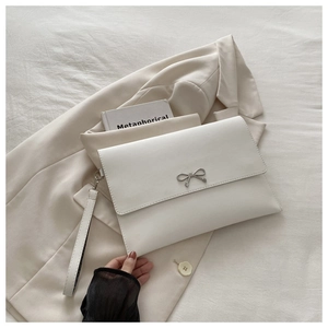 Detail of a white envelope clutch bag with a silver metal bow and detachable wrist strap