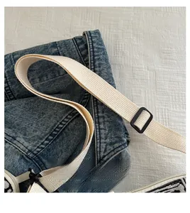 Dettaglio della tracolla regolabile crema con fibbia nera su borsa in denim blu