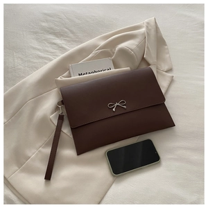 Detail of dark brown envelope clutch with bow metal clasp on a beige blazer