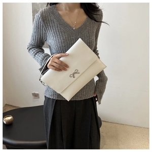 Close-up of white leather envelope bag featuring a silver metal bow accent and fine texture
