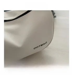 Close-up of cream crossbody bag featuring fine twill texture and black OOTMAO logo print