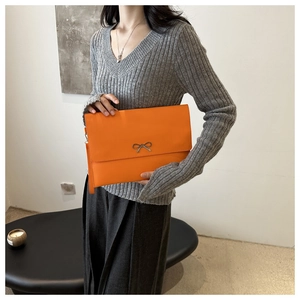 Detail of bright orange envelope clutch with metallic bow and wrist strap on a model