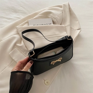 Chic black leather shoulder bag with a gold bow accent on a cream blazer background