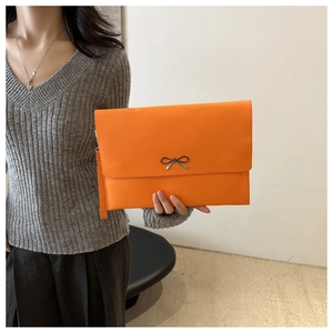 Close-up of bright orange envelope clutch bag with black bow and wrist strap accessory