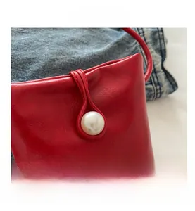 Gros plan sur un sac carré en cuir rouge avec boucle perle blanche et texture raffinée