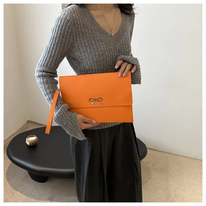 Close-up of bright orange envelope clutch with silver metal bow and leather wristlet