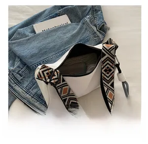 Spacious interior of white dumpling bag with colorful geometric woven strap and essentials
