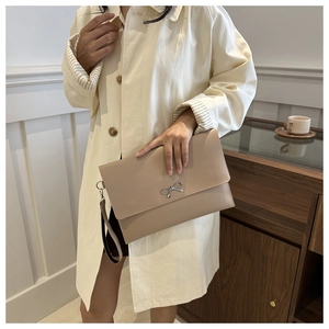 Detailed view of beige envelope clutch bag with silver bow accent and detachable wristlet
