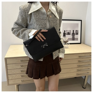 Detail view of a black leather clutch featuring a silver bow buckle and wrist strap