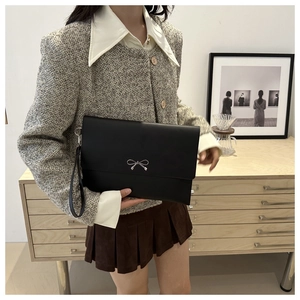 Detail of black leather envelope clutch with silver bow metal clasp and wrist strap