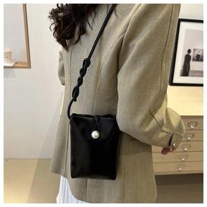 Détail d'un mini sac bandoulière en cuir noir avec bouton perle et bandoulière tressée