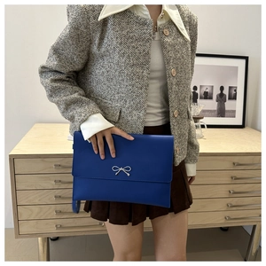 Detail of royal blue envelope clutch featuring a silver bow metal accessory in hand