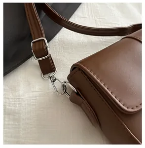 Dettaglio del gancio in metallo argento e tracolla di una borsa in pelle marrone