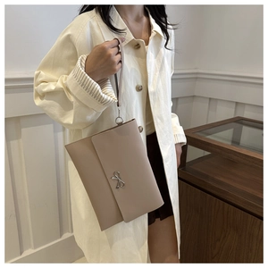 Detail of light beige envelope clutch with silver bow charm and wristlet strap