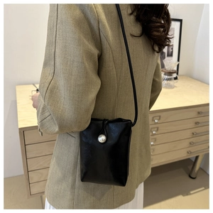 Gros plan sur un mini sac à bandoulière noir avec un bouton perle élégant en détail