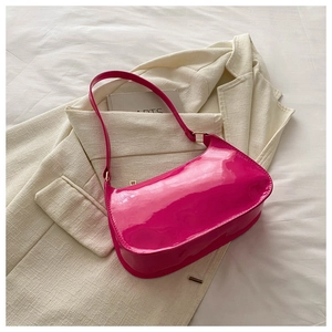 Detail of bright pink patent leather hobo bag with gold buckle on white fabric