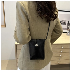 Rear view of a mini black crossbody bag with a large pearl clasp worn by a model