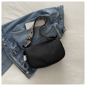 Detail of waterproof nylon dumpling bag with patterned woven strap on denim background