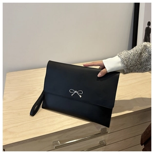 Close-up of minimalist black leather clutch with silver metal bow and wrist strap