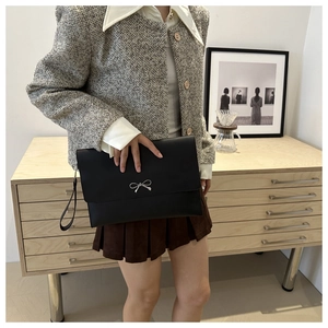 Detail of black leather envelope clutch featuring a silver metal bow and wrist strap