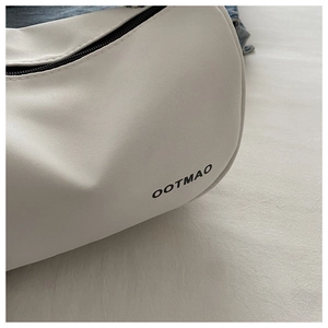 Detail view of the ivory dumpling bag showing fine twill texture and black OOTMAO logo