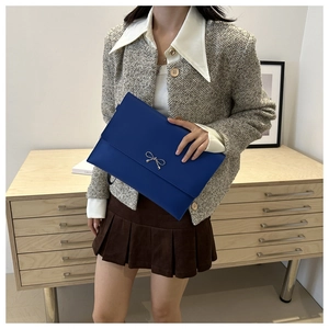 Detail of blue matte leather envelope clutch with a silver bow ornament on a stylish model