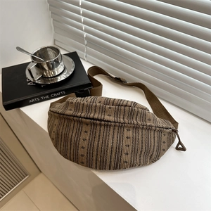 Brown woven crossbody chest bag with textured stripes and adjustable strap on a white ledge