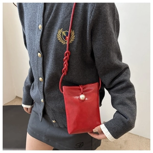 Détail du mini sac bandoulière rouge avec bouton perle sur gilet gris