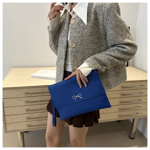 Detail of bright blue leather envelope clutch bag with silver bow and hand strap