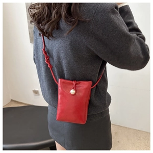Dettaglio mini borsa da telefono rossa in pelle lucida con bottone a perla sulla tracolla