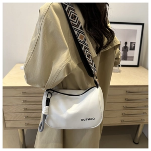 Detail of white half-moon crossbody bag featuring a wide geometric woven shoulder strap