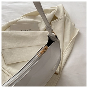 Close-up of a white patent leather baguette bag with shiny finish and golden zipper