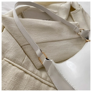 Close-up of white glossy baguette bag with gold hardware on textured fabric